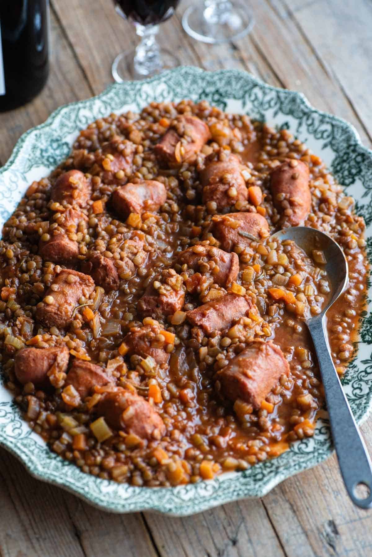 Italian sausages and lentils on a large serving plate sitting on a wooden table.
