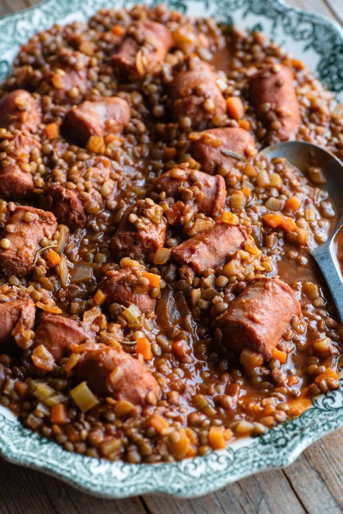 A close up of Italian sausages and lentils on a large plate with a serving spoon.