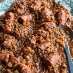 Italian sausages and lentils on a serving plate with a serving spoon.