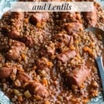 Italian sausages and lentils on a serving plate with a serving spoon.