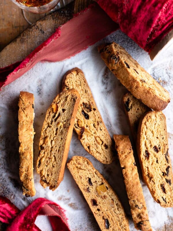 An overhead shot of panettone biscotti on a wooden surface with sugar and a red Christmas ribbon.