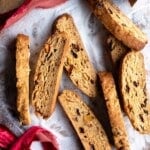 A cropped square image of cantucci biscotti on a wooden surface dusted in sugar.
