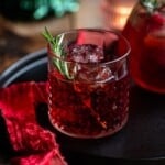 A close up cropped image of a red Italian cocktail in a short glass with a rosemary sprig.