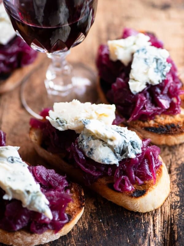 A close up of red onion and gorgonzola crostini on a wooden serving board.