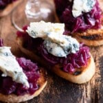 A close up cropped image of red onion crostini topped with gorgonzola cheese.