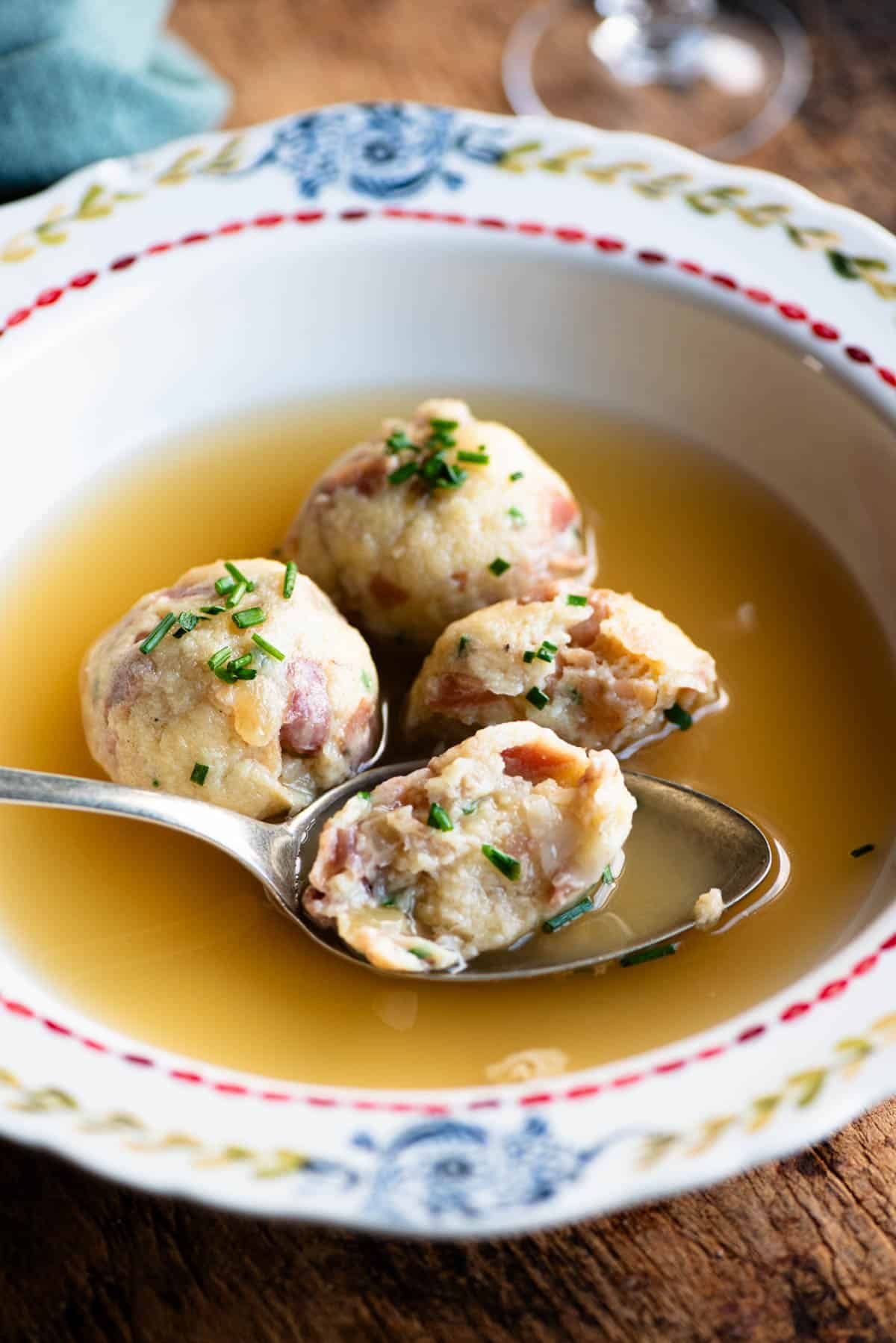 A side shot of canederli dumplings in broth with a spoons.