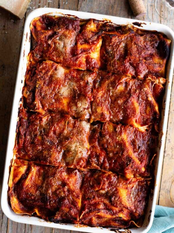 An overhead shot of a Neapolitan lasagna sitting on a wooden table with a bottle of wine at the side.