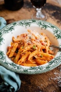 A bowl of penne pasta with a creamy tomato Tuscan sauce on a wooden background with a blue napkin at the side.