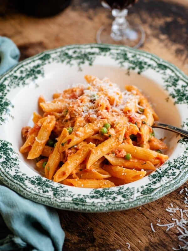 A bowl of penne pasta with a creamy tomato Tuscan sauce on a wooden background with a blue napkin at the side.