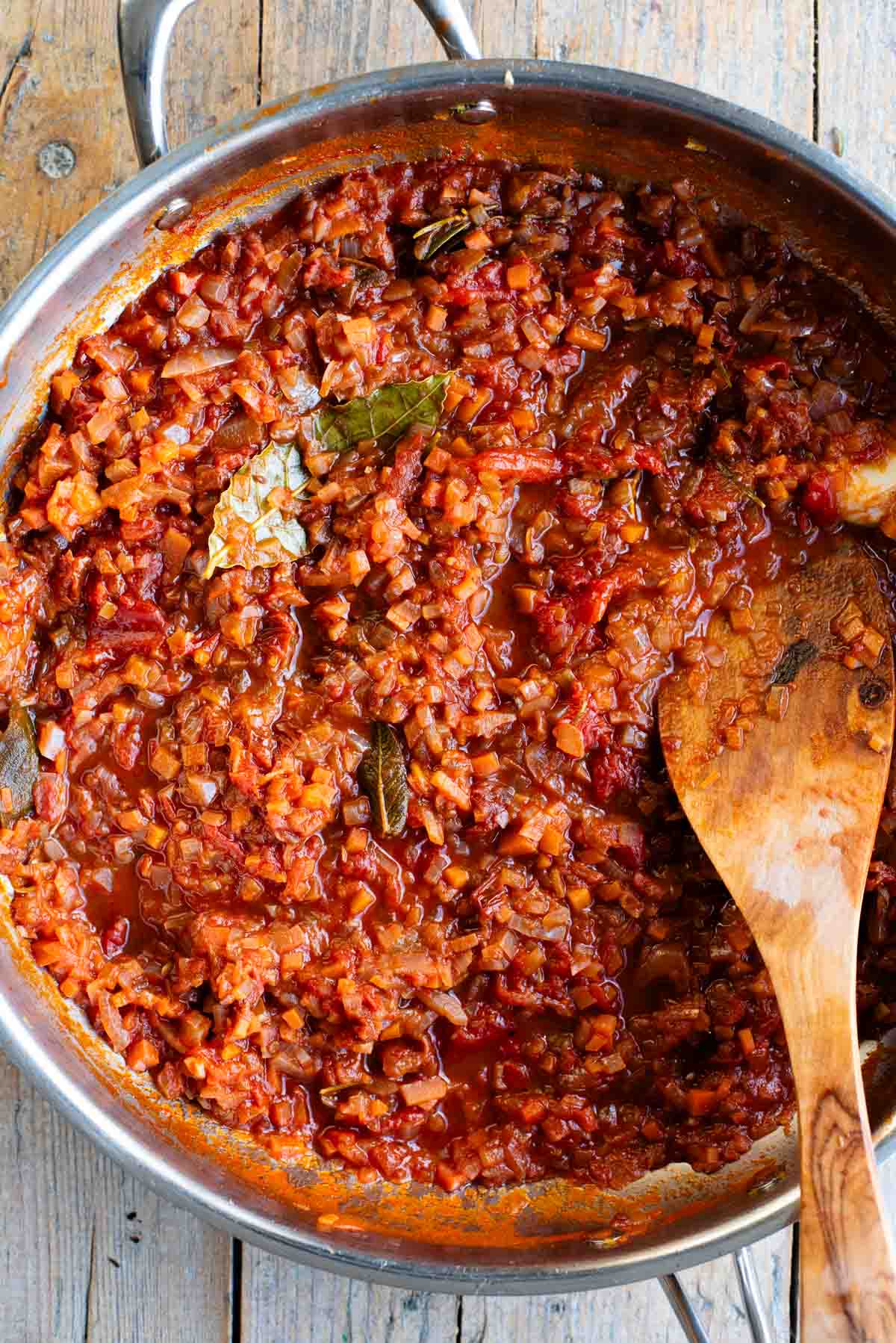 An overhead shot of a skillet with an Italian slow cooked vegetable sauce sitting on a wooden table.