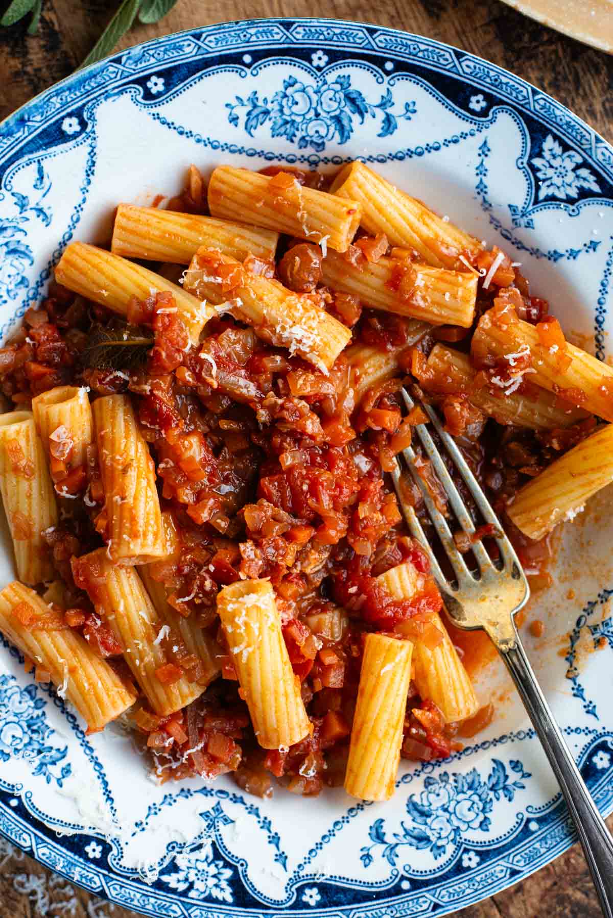 An overhead shot of rigatoni pasta with a vegetable sauce in a blue and white bowl.