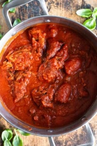 An overhead shot of Sugo Napoletano (Neapolitan ragu) in a large pot sitting on a wooden surface.