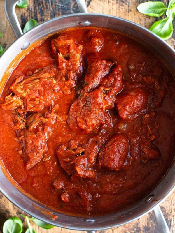 An overhead shot of Sugo Napoletano (Neapolitan ragu) in a large pot sitting on a wooden surface.