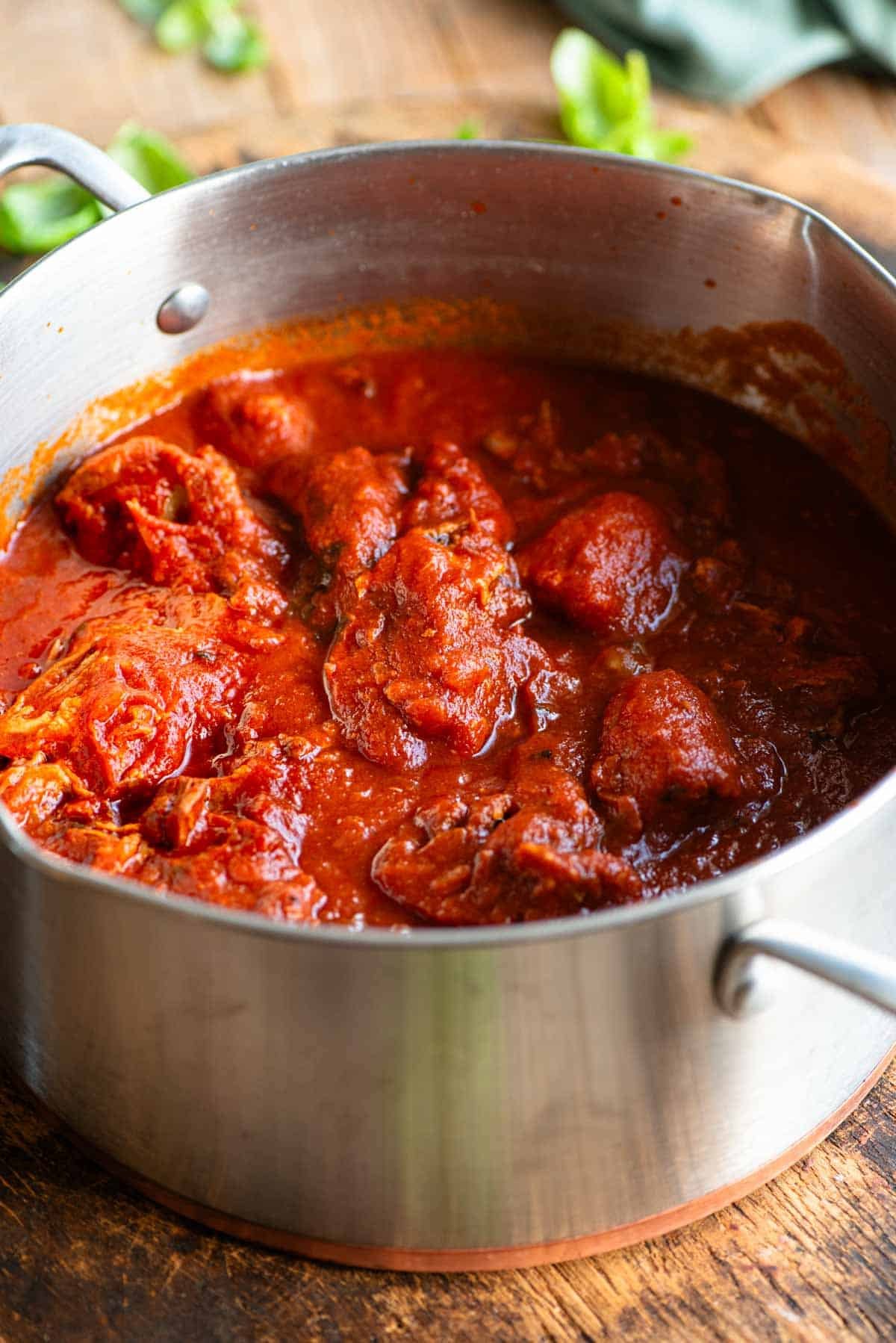 A side shot of Neapolitan ragu in a large pot sitting on a wooden surface.