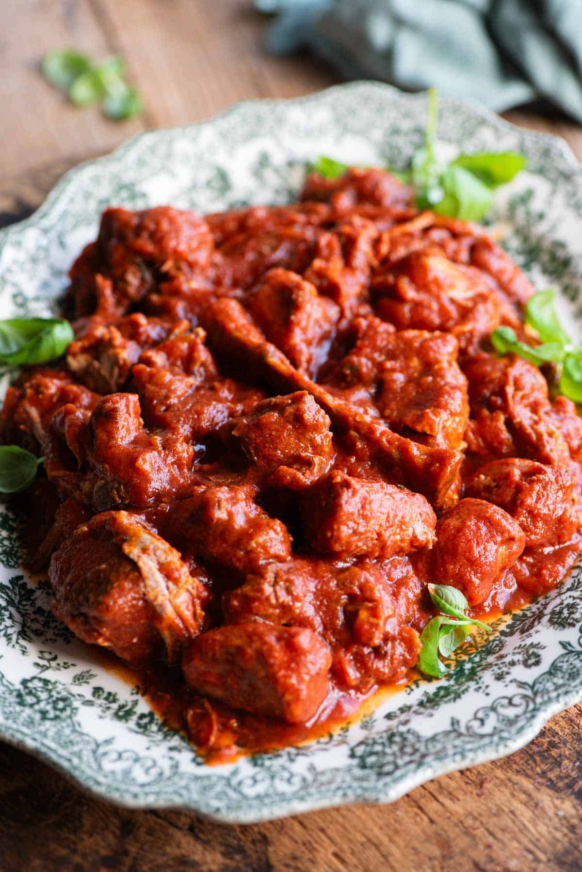 A side shot of lots of cooked meat in tomato sauce on a large serving plate.