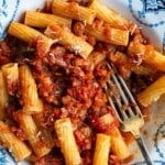 A close up of a rigatoni pasta with a vegetable sauce in a blue and white bowl.