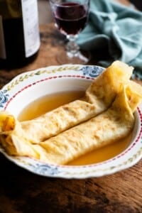 A side shot of Italian crepes in broth in a bowl on a rustic wooden board.