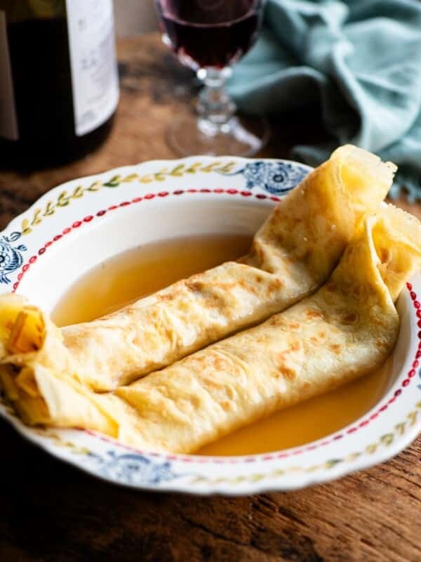 A side shot of Italian crepes in broth in a bowl on a rustic wooden board.