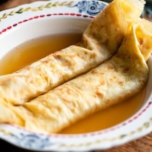 A square cropped image of two crepes in a bowl with broth.