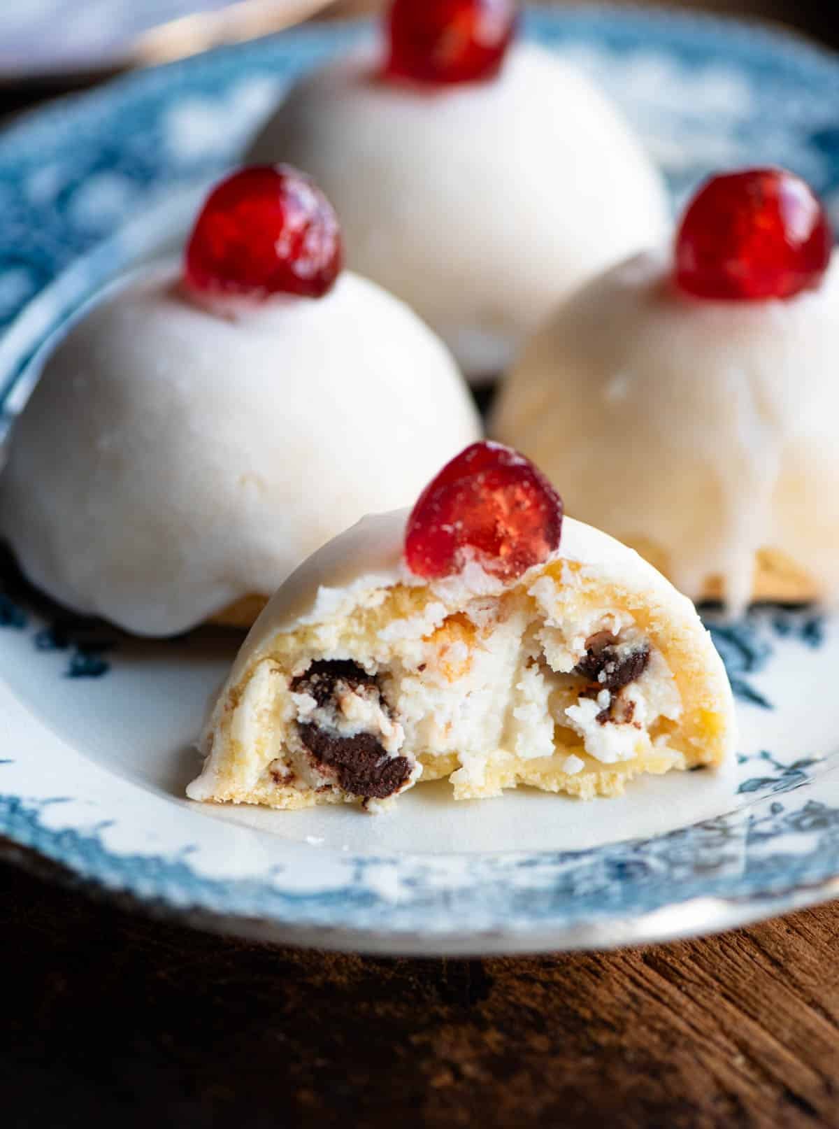 A close up of a Sicilian pastry cut in half showing a ricotta filling with chocolate chips and candied fruit.