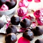 A close up cropped image of homemade baci chocolates in pink foils on a travertine worktop.