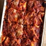 An overhead shot of a Neapolitan lasagna cut into slices in a baking dish.