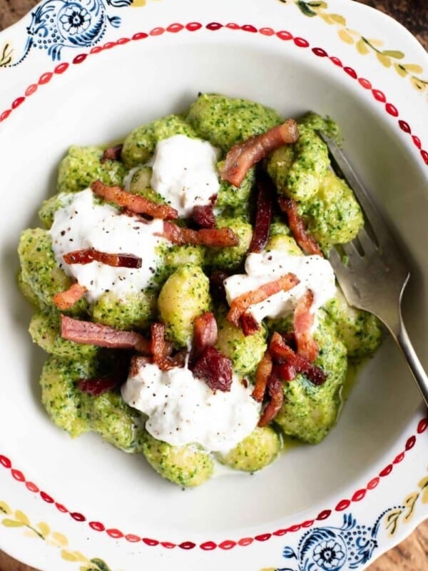 An overhead shot of a bowl of arugula pesto gnocchi topped with burrata cheese and crispy pancetta.