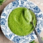 A cropped image of arugula pesto in a blue and white bowl with a spoon.