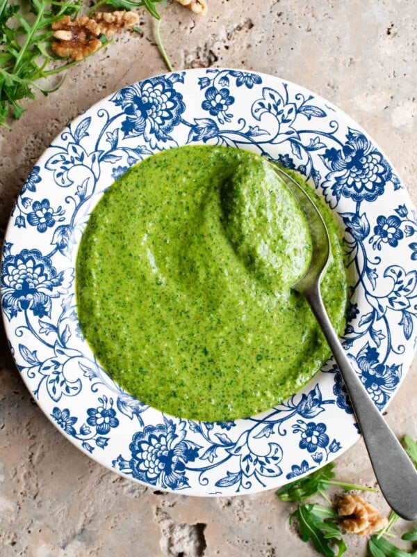 An overhead shot of arugula pesto in a blue and white patterned bowl with a spoon at the side.