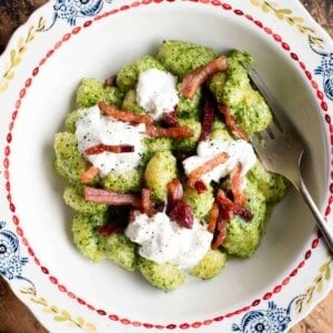 An cropped image of arugula pesto gnocchi in a bowl topped with pancetta and burrata.