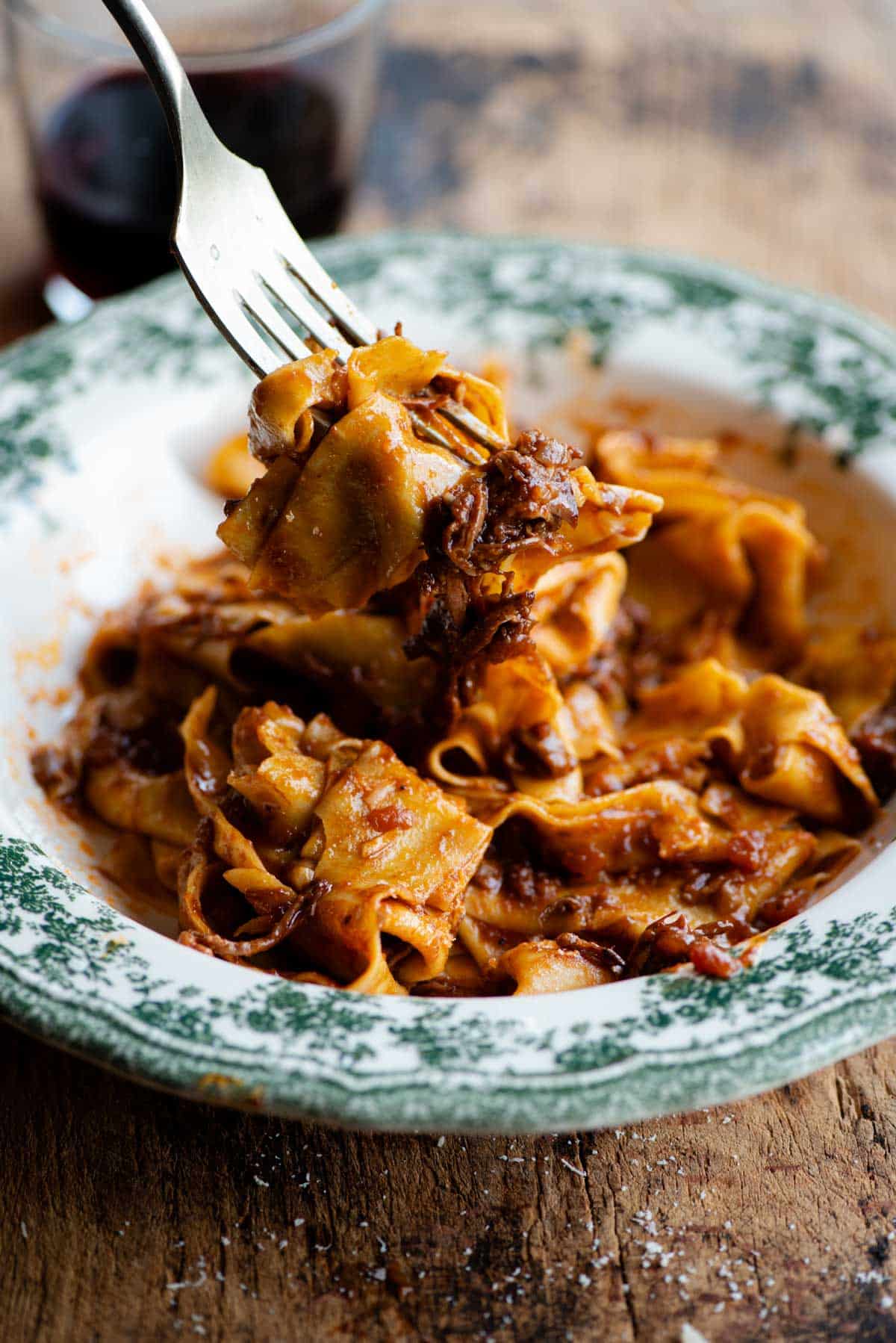 A side shot of a fork picking up some beef ragu and pappardelle pasta.