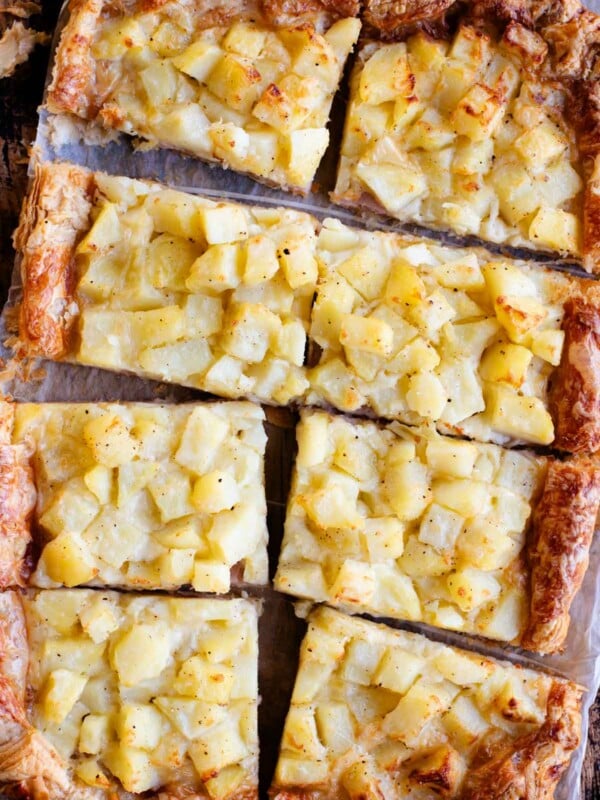 An overhead shot of a puff pastry tart topped with potatoes, ham and cheese and cut into 8 slices.