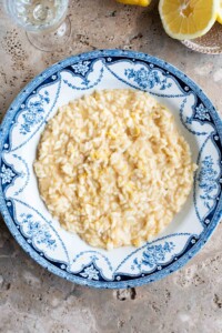 An overhead shot of a bowl of lemon risotto on a travertine surface with lemons at the side.