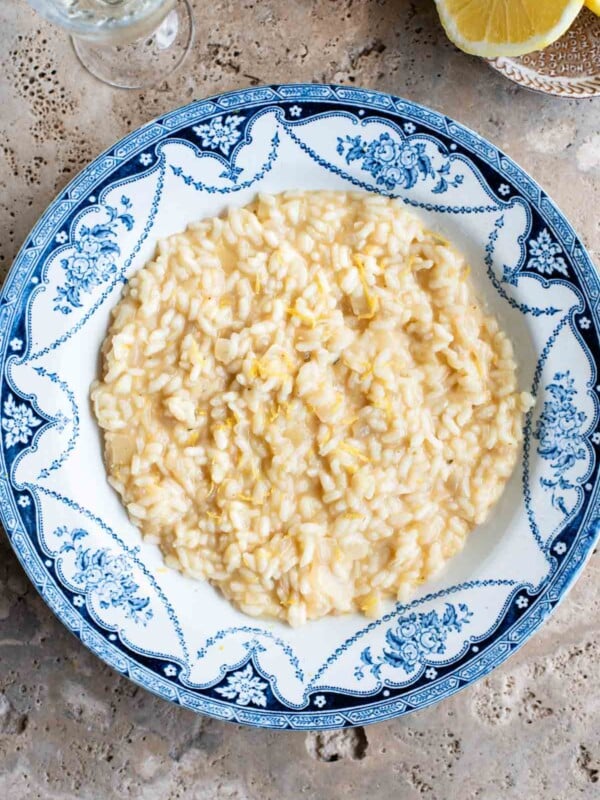 An overhead shot of a bowl of lemon risotto on a travertine surface with lemons at the side.