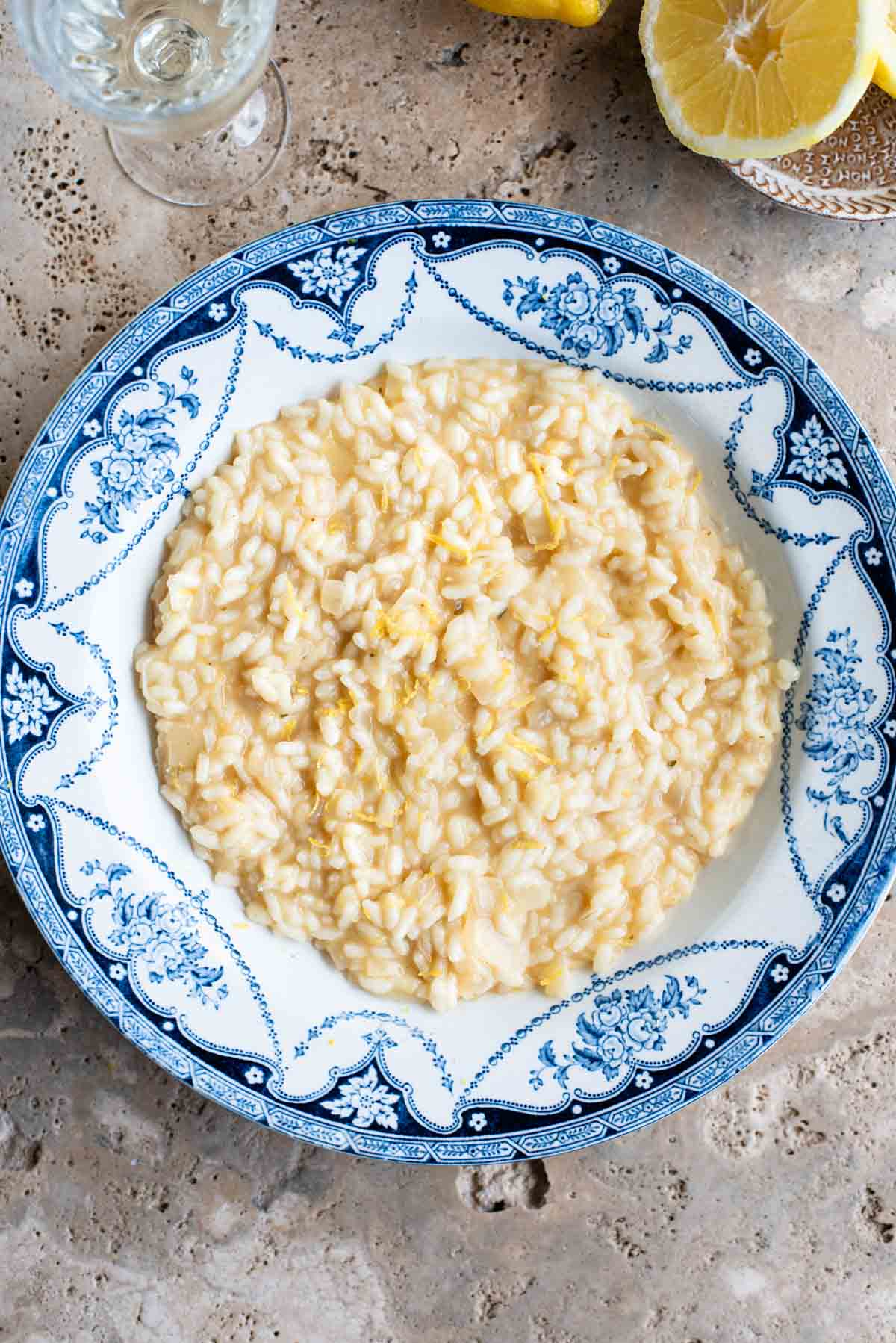 An overhead shot of a bowl of lemon risotto on a travertine surface with lemons at the side.