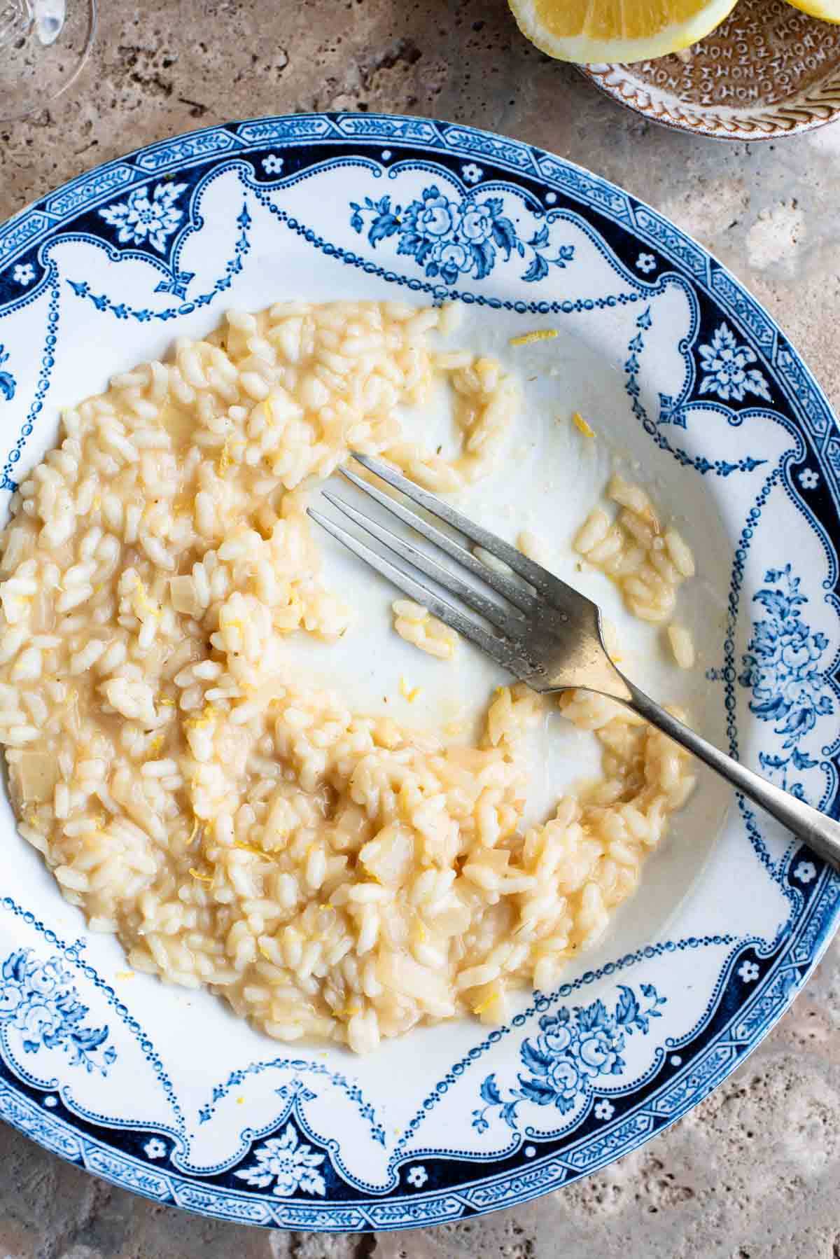 An overhead close up of a bowl of lemon risotto that's half eaten with a fork sitting in the bowl.