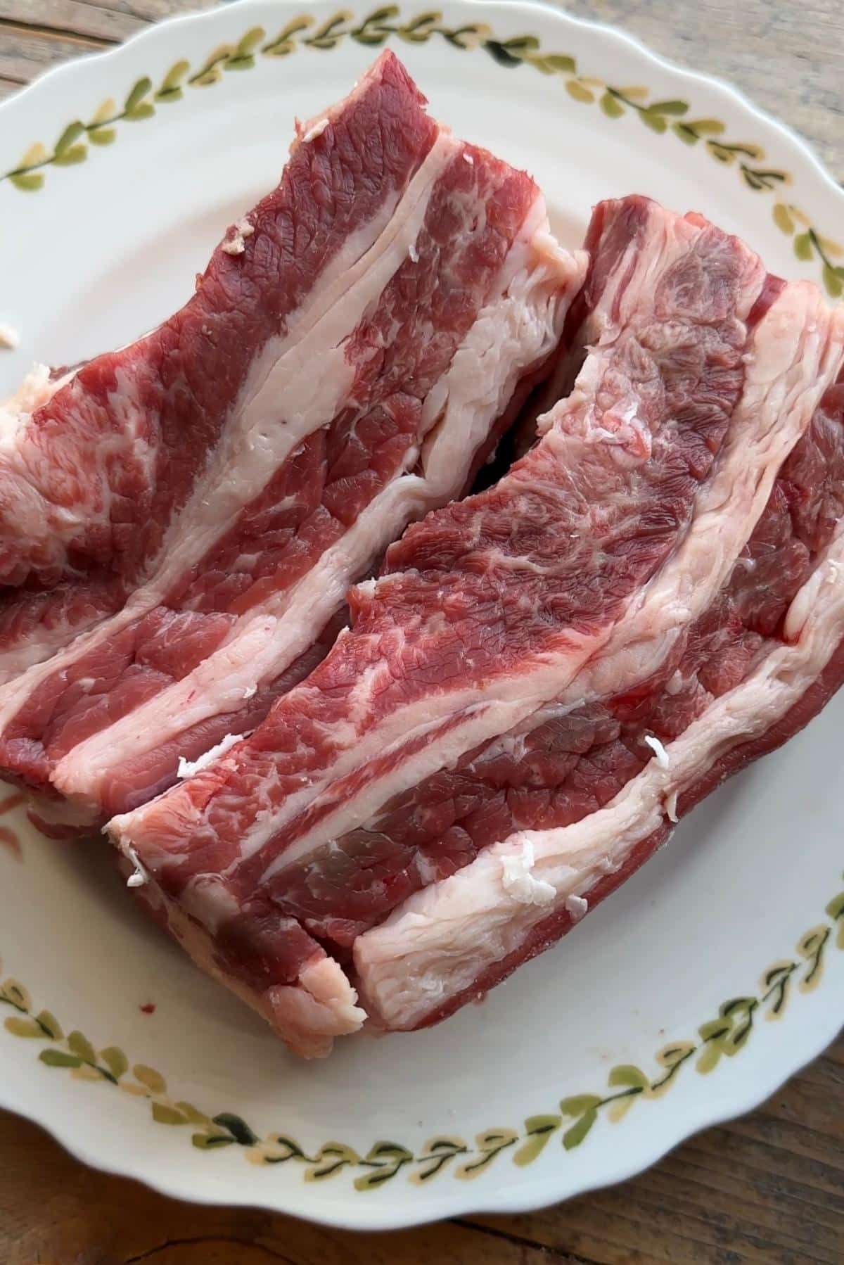 A close up of two beef short ribs on a plate with the lifter muscle attached.