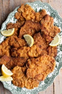 Slices of breaded pork fillet on a serving plate with slices of lemon. The plate is green and white.