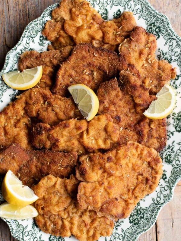 Slices of breaded pork fillet on a serving plate with slices of lemon. The plate is green and white.