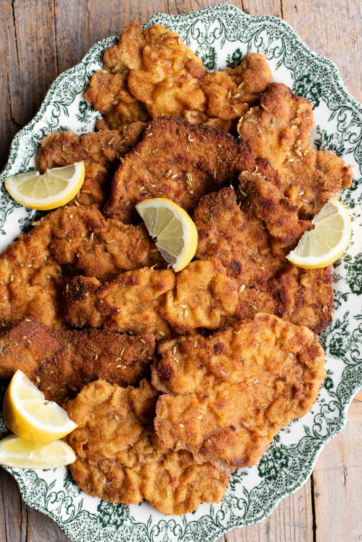 Slices of breaded pork fillet on a serving plate with slices of lemon. The plate is green and white.