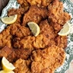A close up of breaded pork cutlets on a serving plate with lemon wedges.