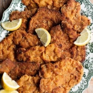 A close up of breaded pork cutlets on a serving plate with lemon wedges.