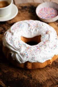 An Italian bundt cake on a wooden board topped with meringue and sprinkles.