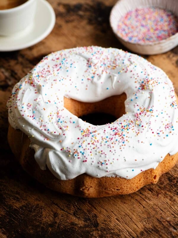 An Italian bundt cake on a wooden board topped with meringue and sprinkles.