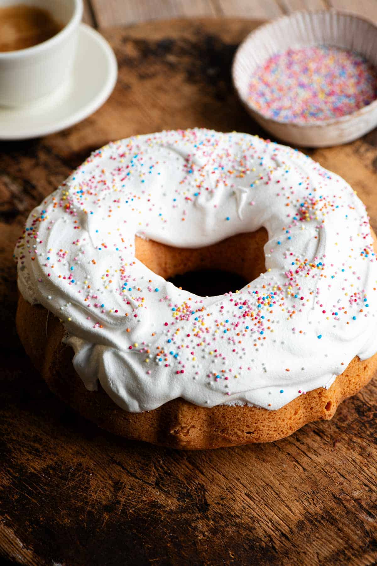 An Italian bundt cake on a wooden board topped with meringue and sprinkles.