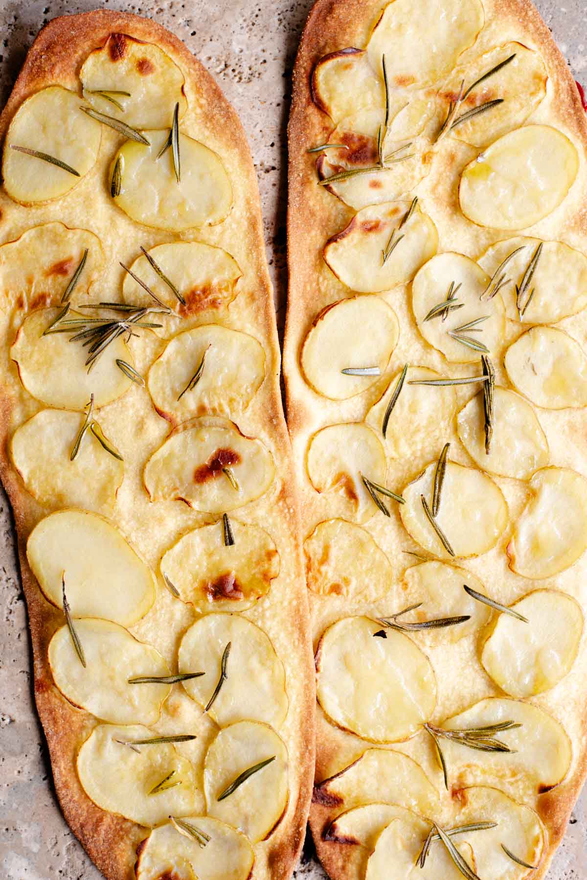 Two long and thin pizzas with slices of potato and rosemary on top.