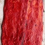 A close up of two long and thin crispy pizzas covered in tomato sauce.