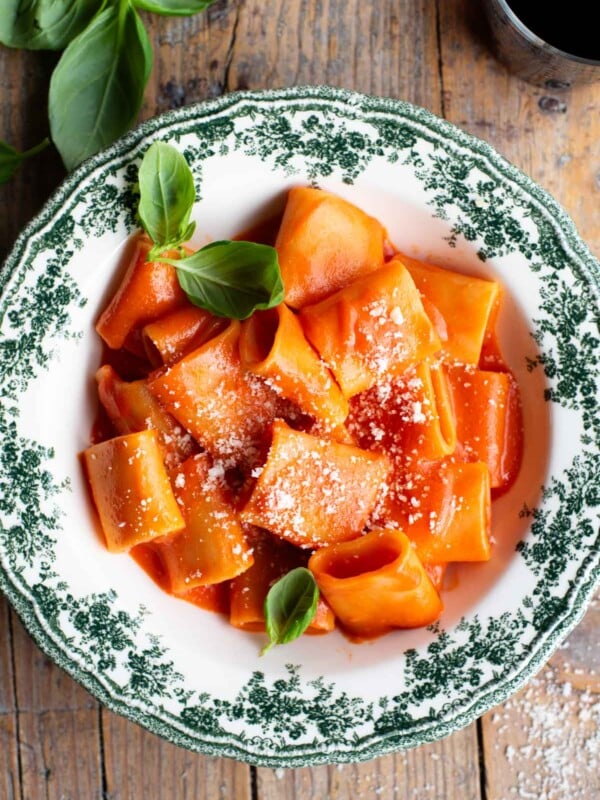 Paccheri pasta with a smooth tomato sauce in a green and white patterned bowl topped with basil.