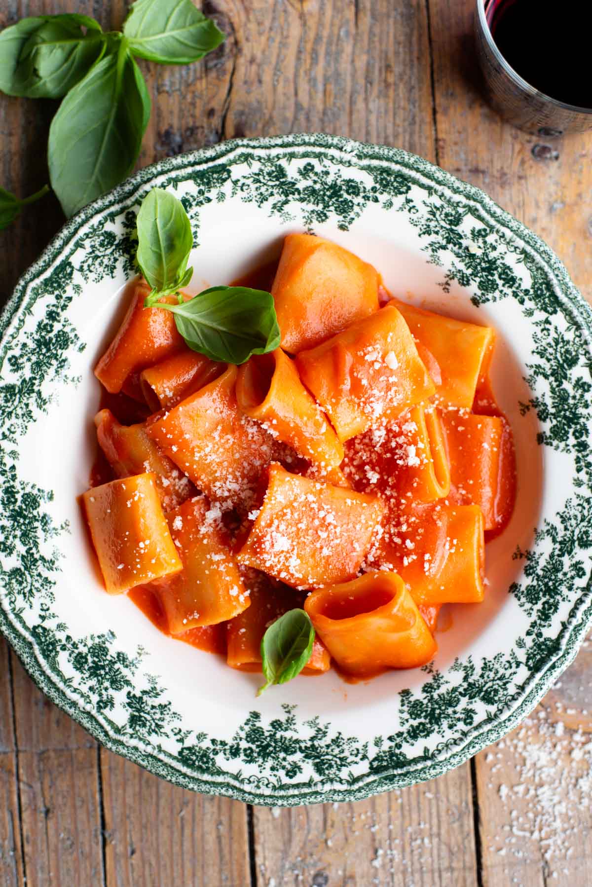Paccheri pasta with a smooth tomato sauce in a green and white patterned bowl topped with basil.