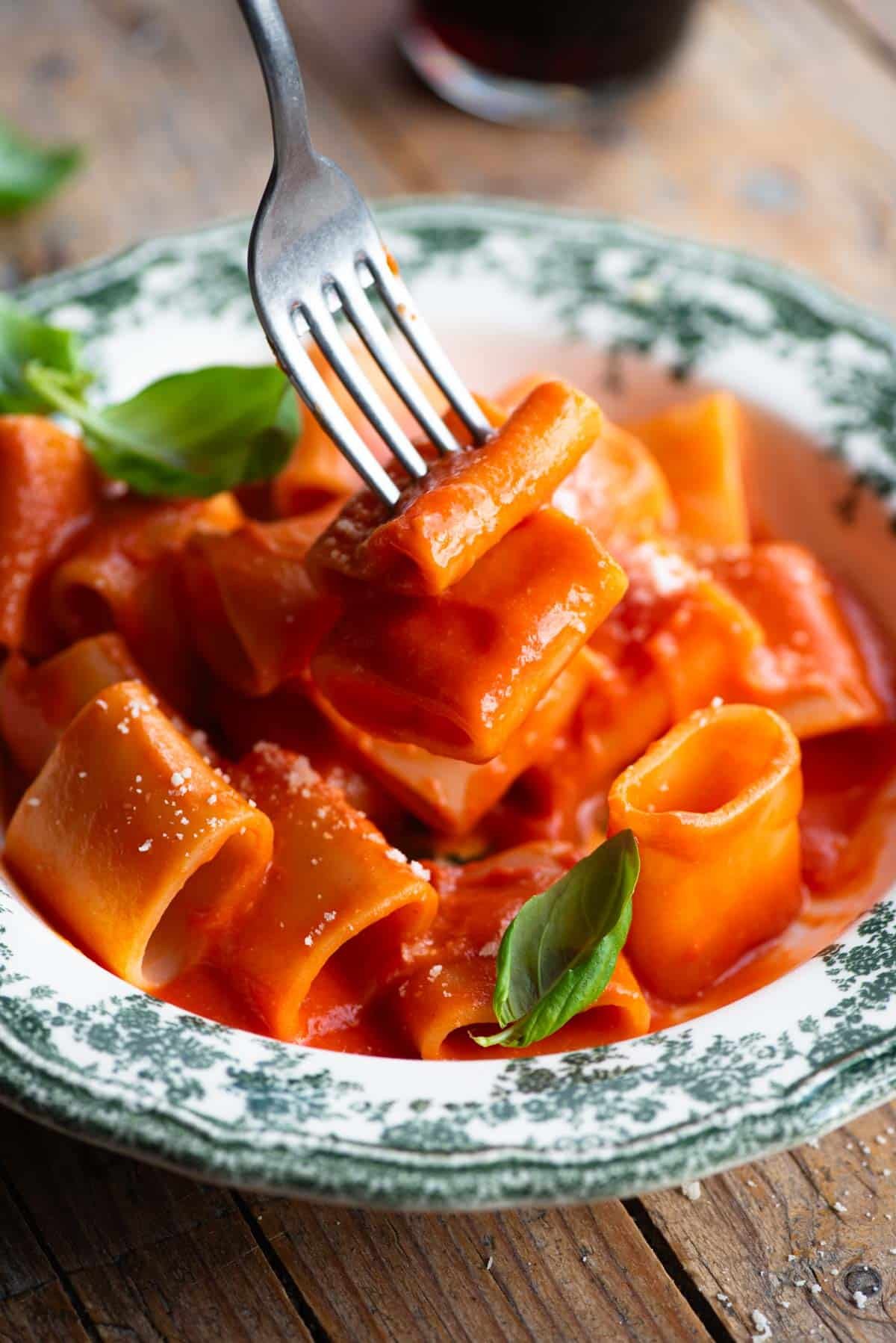 A close up of a fork picking up paccheri pasta with tomato sauce.